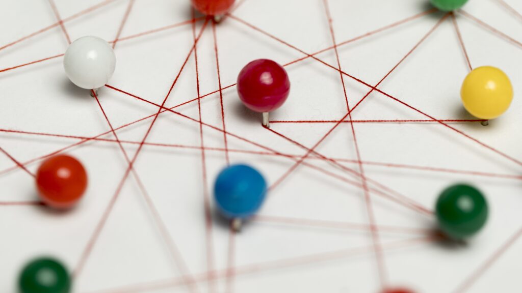 Pushpins in various colours connected by a red thread, illustrating a complex network